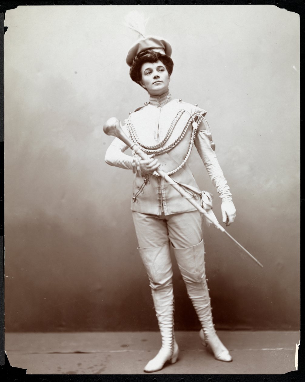 Une femme modélisant un uniforme de fanfare, tenant un bâton, vers 1898 - Byron Company