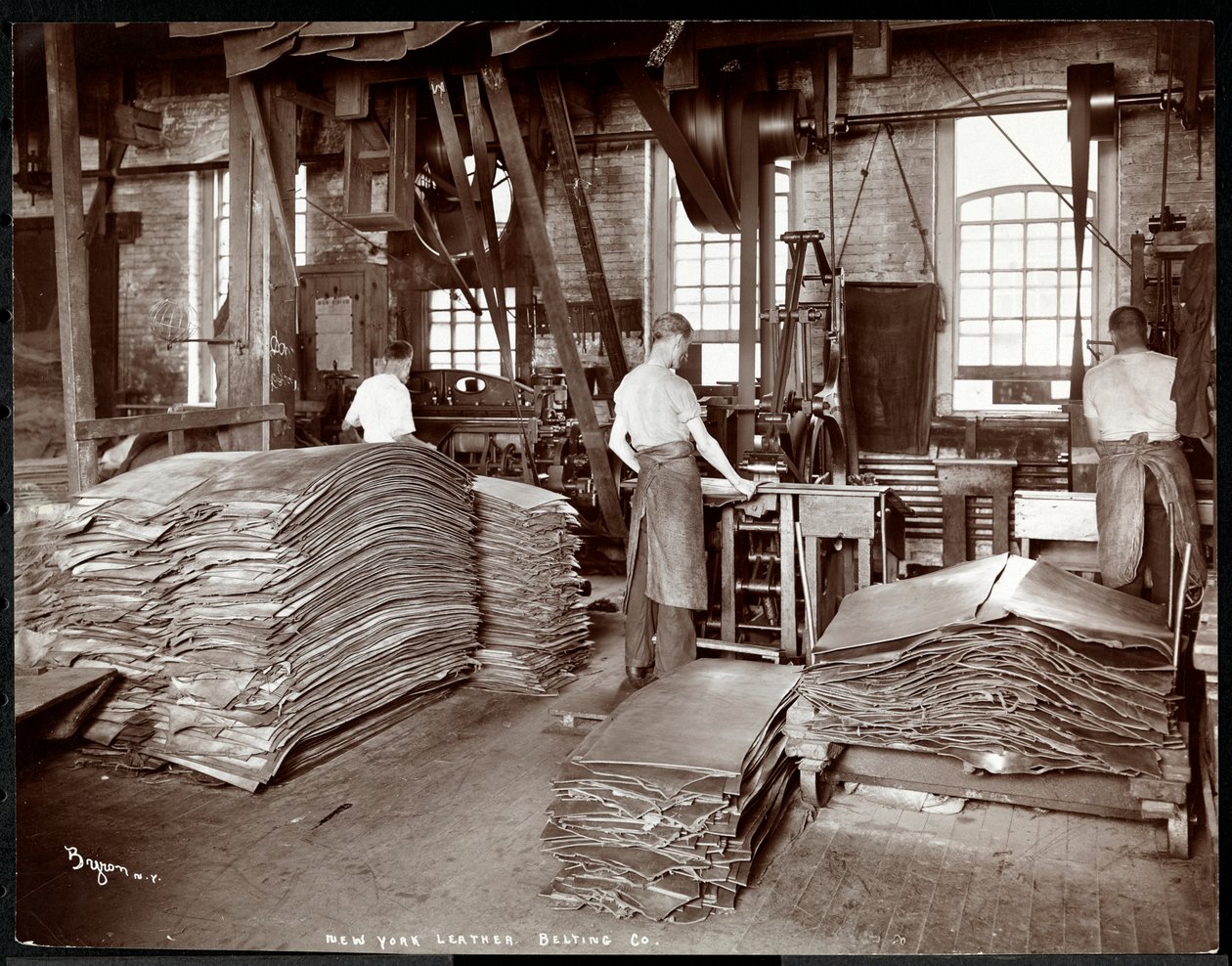 Vue intérieure de trois hommes travaillant le cuir et des équipements lourds à la New York Leather Belting Co., New York, 1905 - Byron Company