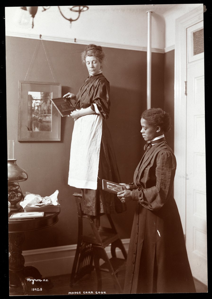 Madge Carr Cook accrochant des tableaux avec sa domestique, vers 1904 - Byron Company